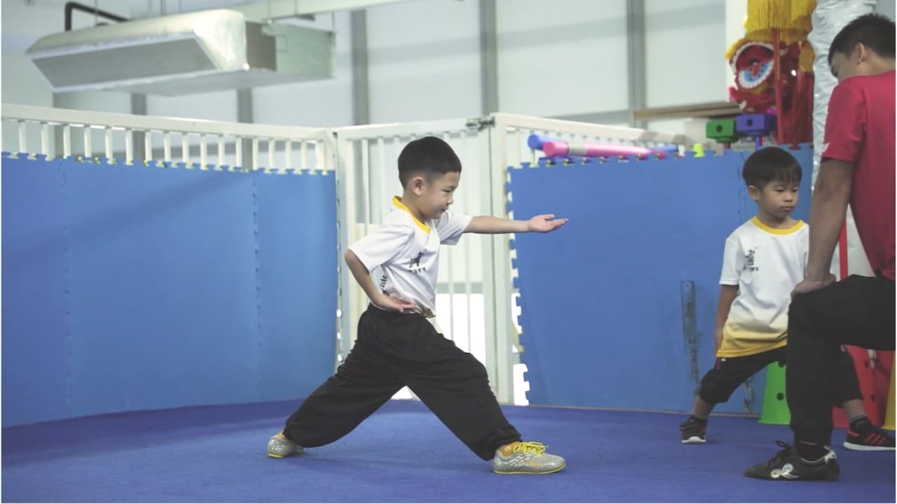 Young Sino Wushu student executing a focused horse stance under the watch of his instructor